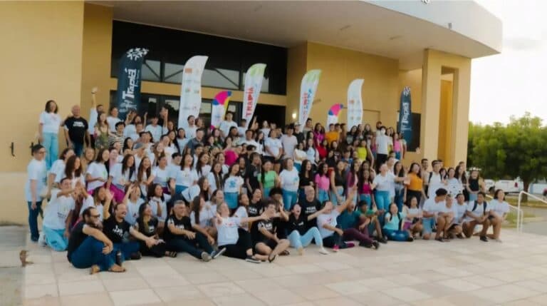 Grande grupo reunido em frente a teatro, todos sorrindo e levantando as mãos.