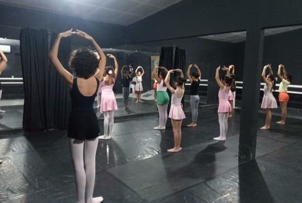 Meninas em aula de balé, usando tutus e sapatilhas, aprendendo passos de dança.